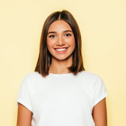 Young beautiful woman looking at camera.Trendy girl in casual summer white T-shirt and jeans shorts.Positive female shows facial emotions.Funny model isolated on yellow